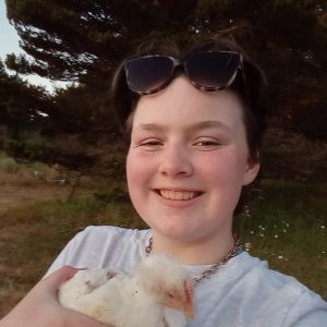 Smiling Liesl with sunglasses on her head, holding a yellow fluffy chicken under her chin.