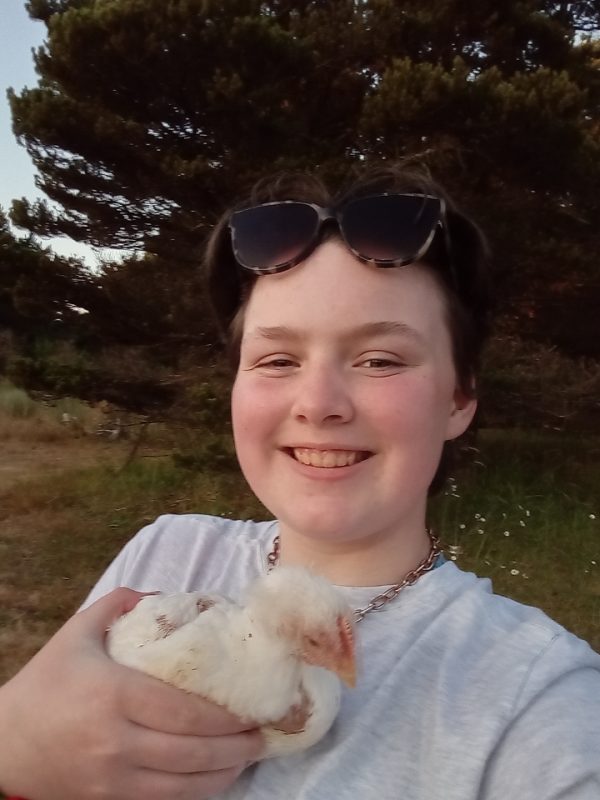 Smiling Liesl with sunglasses on her head, holding a yellow fluffy chicken under her chin.