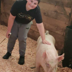 Smiling Daniel leaning down with a hand on the back of his pig, Snoop Hog.