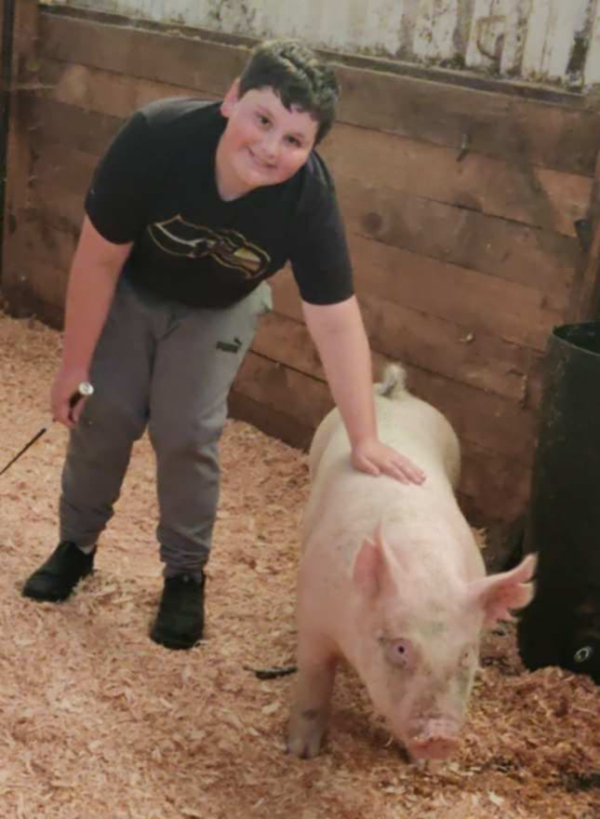 Smiling Daniel leaning down with a hand on the back of his pig, Snoop Hog.