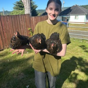 Brooke with her 3 pullets in her arms standing in front of a fence.