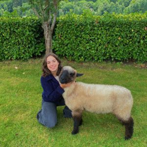 Lorelei kneeling on a lawn next to her lamb, Walter.