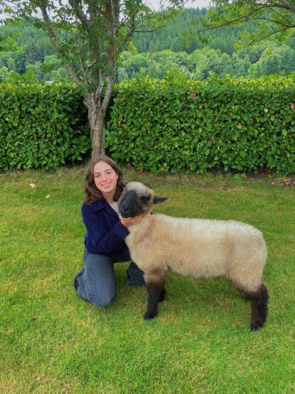 Lorelei kneeling on a lawn next to her lamb, Walter.